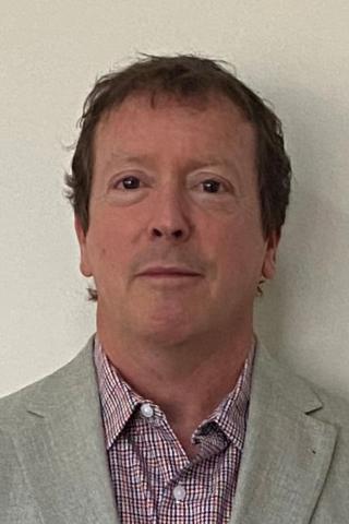 Headshot of a man in a gray blazer over a red and white checkered shirt.