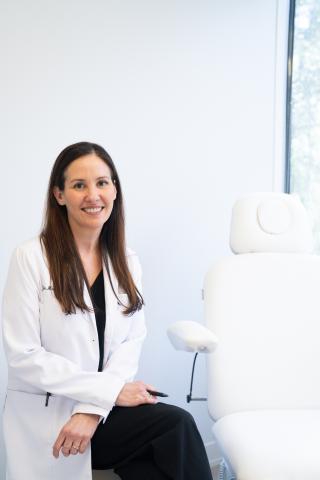 Woman in white lab coat smiling next to a medical chair.