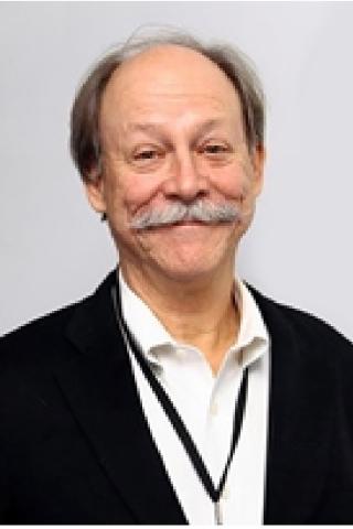 Portrait of an older man with gray hair, mustache, wearing a black blazer over a white shirt.