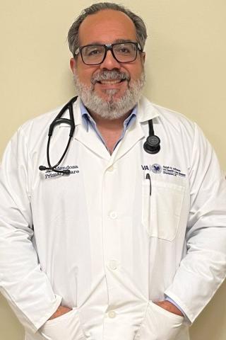 Male doctor in white coat with stethoscope around neck, smiling.