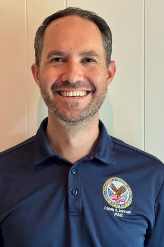 Man in blue polo shirt with logo smiling at camera.