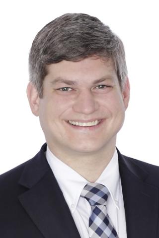 Portrait of a smiling man in a dark suit and blue plaid tie.