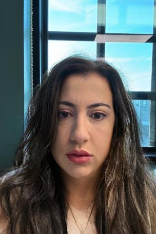 Woman with long dark hair and red lipstick, in front of a window.