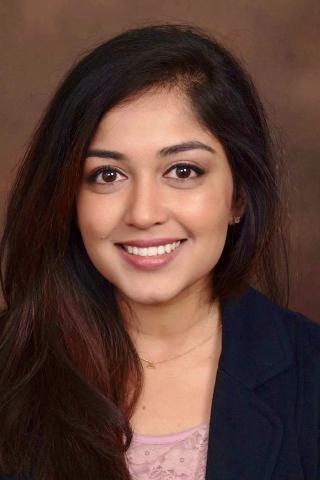 Woman with long black hair, pink top, and navy blazer smiling for the camera.