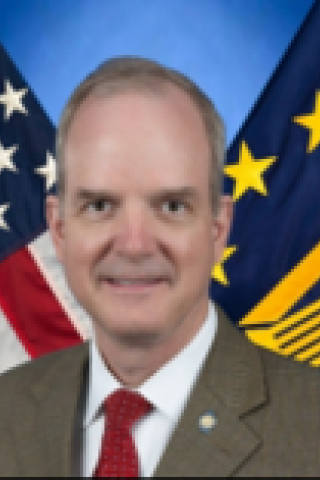 Smiling man in suit with American and European Union flags in background.