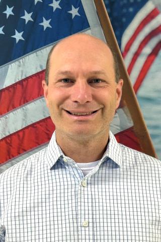 Portrait of smiling man in a white shirt against American flag background.