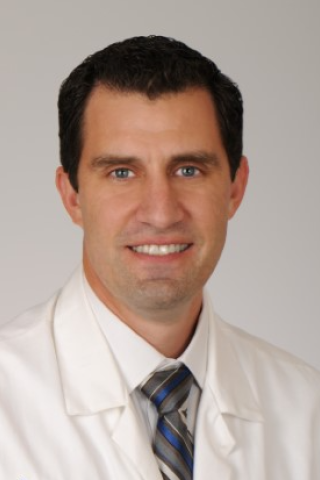 Smiling man in white lab coat and striped tie.