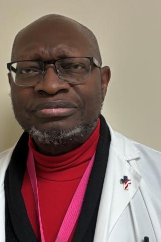 A bald man in a red turtleneck and white coat, looking at the camera.
