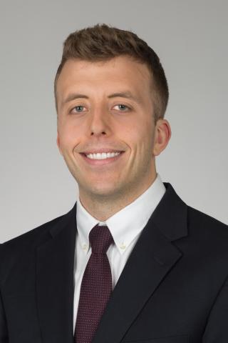 Man in black suit and maroon tie smiling at camera.