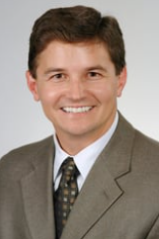 Headshot of a man in a suit and tie smiling.