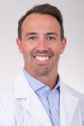 Portrait of a man in a white lab coat smiling.