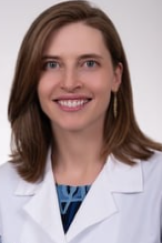 Woman in white lab coat and blue shirt smiling.