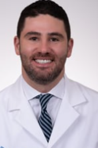 Male doctor in white lab coat and striped tie smiling.