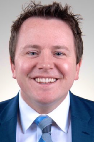 Headshot of a man in a blue suit and tie smiling.