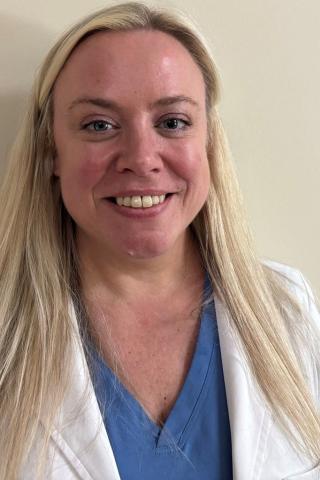 Photo of a smiling woman with blonde hair wearing a white lab coat and blue shirt.