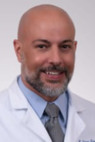 Smiling bald man in white lab coat and gray tie.