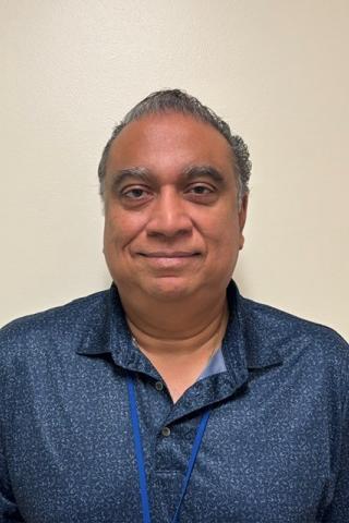 A smiling man in a blue shirt with a blue lanyard around his neck.