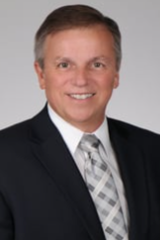 Man in black suit and checkered tie smiling at the camera.
