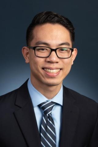 Portrait of a man wearing glasses, suit, and striped tie smiling at the camera.