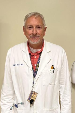 Smiling man in white lab coat with stethoscope around his neck.