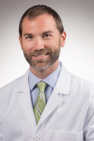 Man in white lab coat and green tie smiling for the camera.