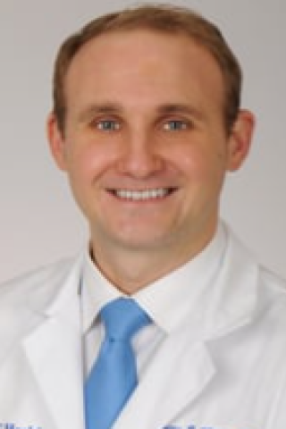 Smiling man in white lab coat and blue tie, headshot.