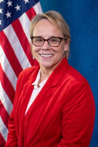 Dr. Woodrum's official VA photo, she is smiling in front of the American flag.