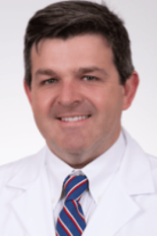 Smiling man in white lab coat and red, white, and blue tie.