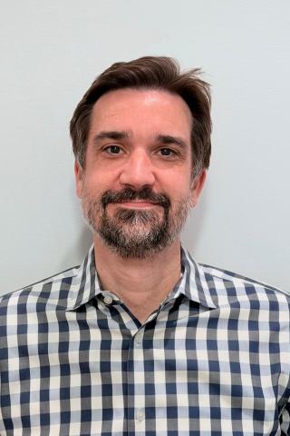 Man with a beard smiling, wearing a blue and white checkered shirt.