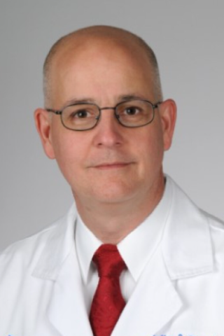 Bald man in white lab coat and red tie.