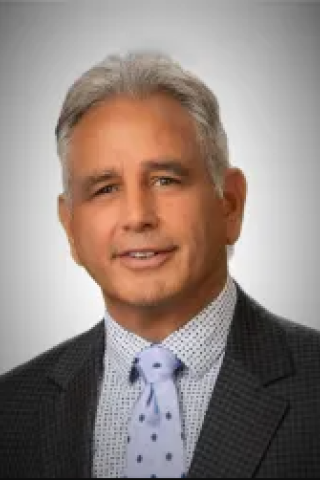 Portrait of a man in a gray suit and blue tie smiling.