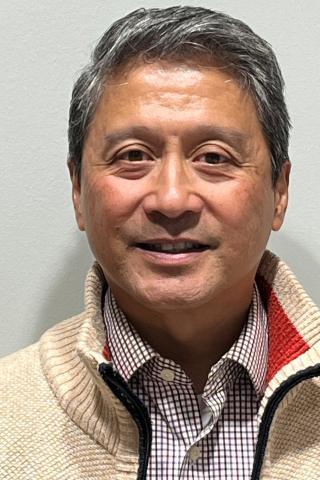Portrait of a man with short grey hair, wearing a beige sweater, smiling.