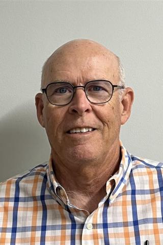 Portrait of a smiling older man in an orange and blue plaid shirt.
