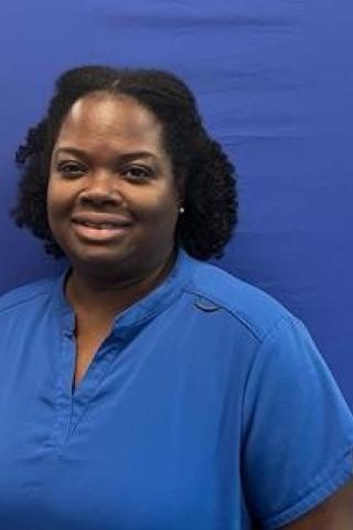 Woman smiling in front of blue backdrop, wearing blue shirt.