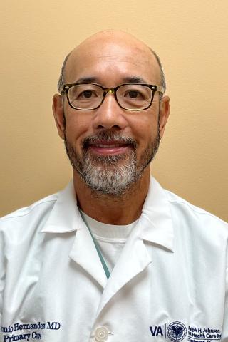 Smiling man in white coat, wearing glasses, with name tag.