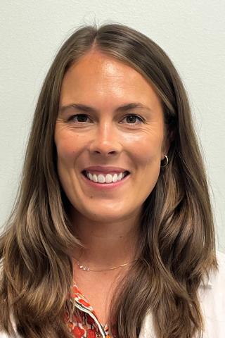 Headshot of smiling woman with brown hair and white lab coat.