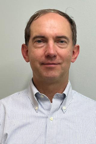 Man in a blue and white checkered shirt smiling at the camera.