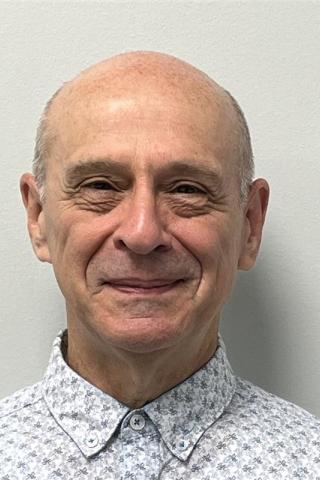Headshot of a bald man wearing a patterned shirt, smiling at the camera.