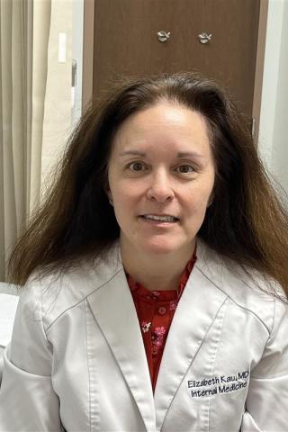Woman in white lab coat over red shirt smiling in front of curtain.