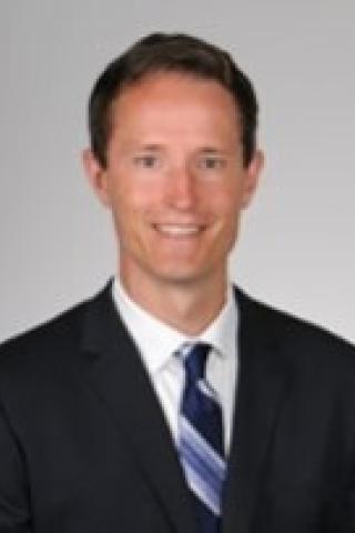 Man in black suit and blue and white striped tie smiling for the camera.