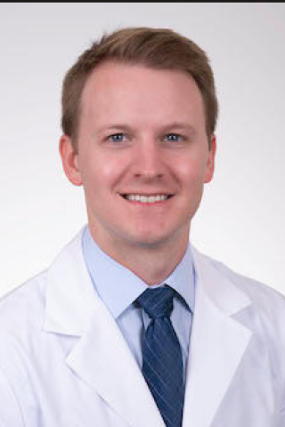 Man in white lab coat and blue tie smiling for the camera.
