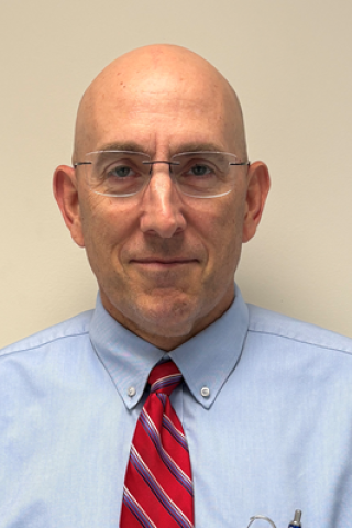 Bald man in blue shirt and red striped tie smiling.