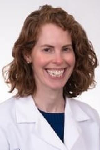 A smiling woman in a white lab coat over a blue shirt, posing for a photo.
