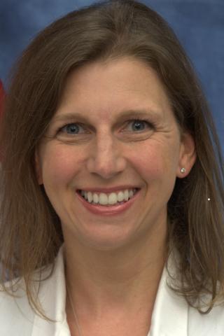 Portrait of a smiling woman with brown hair and blue eyes wearing a white shirt.