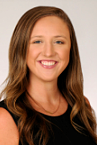 Woman with long brown hair and black top smiling for a photo.