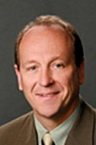 Photo of a man in a suit and green shirt smiling.