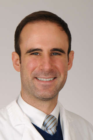 Smiling man in white lab coat and striped tie.