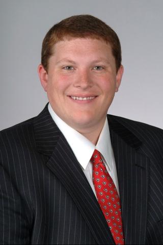 Man in a black pinstripe suit and red tie, smiling.