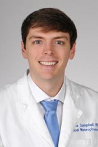 A man in a white lab coat and blue tie smiles for the camera.