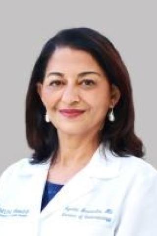 Portrait of a smiling woman in a white lab coat with blue earrings.